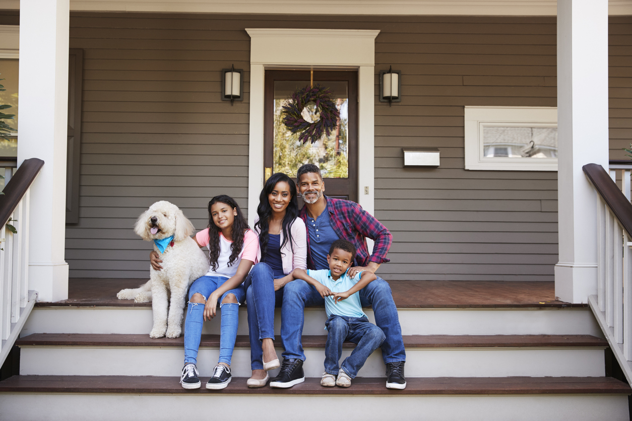 Family With Children And Pet Dog Sit On Steps Of Home